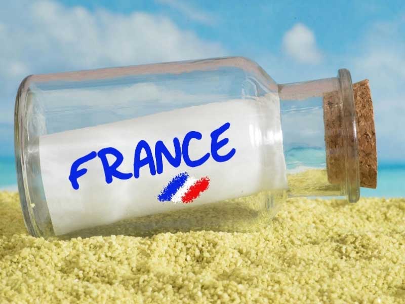 Glass bottle with a piece of paper saying France, on a sandy beach