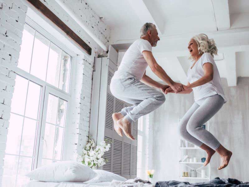Elderly man and woman jumping up and down on a bed