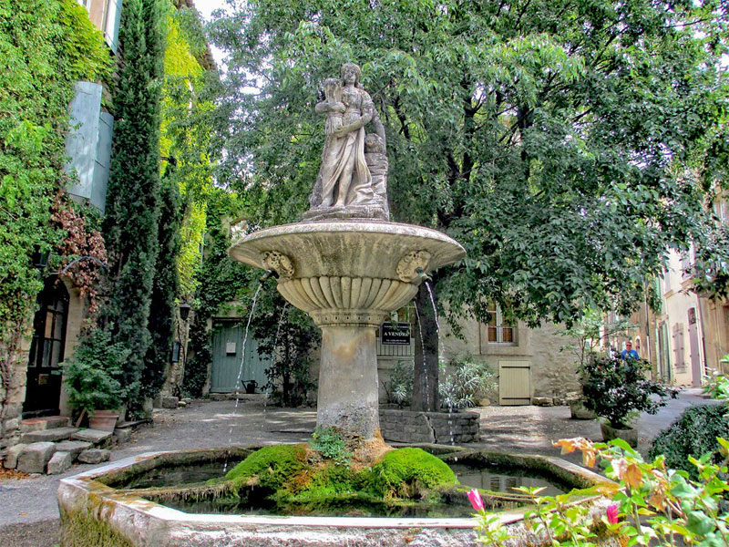 Stone fountain with a statue of a woman, in a small flower filled square in France