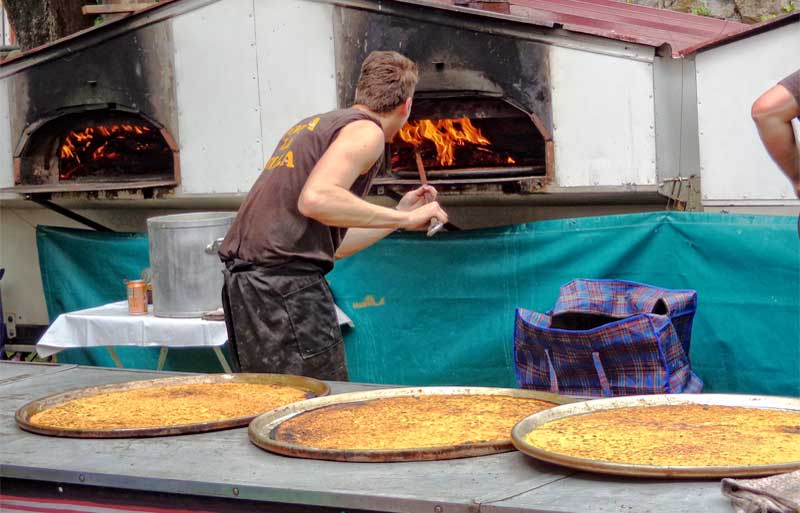 Man making socca, like pancakes made with chickpea flour, in an outdoor wood oven in Nice